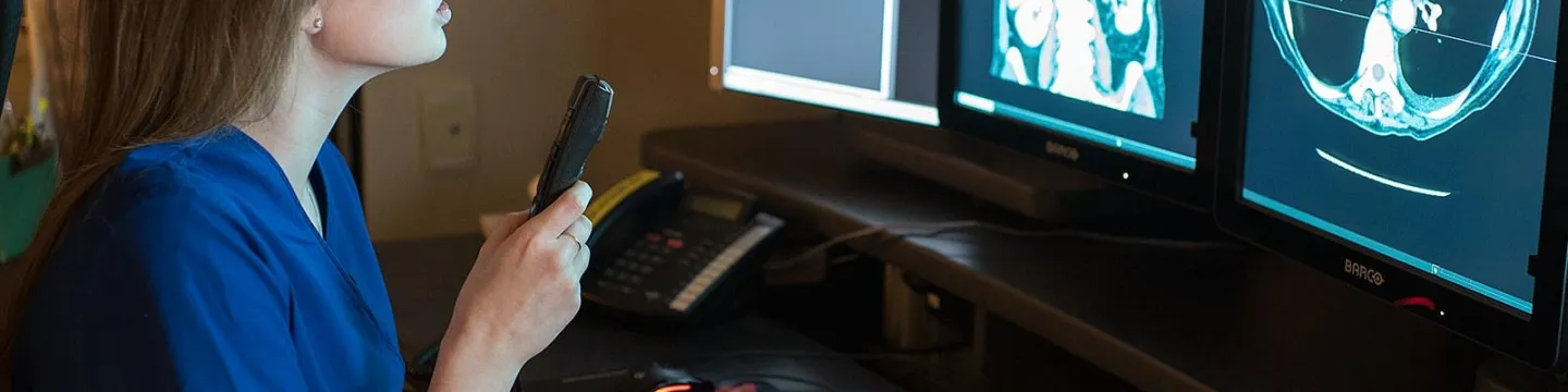 a radiographer reviewing two images on two computer screens