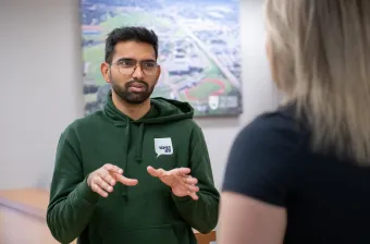 a UPEI student in a green UPEISU hoodie standing in an office